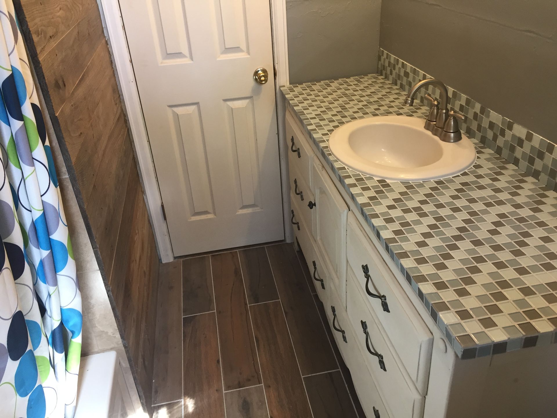 Small bathroom with patterned countertop, white sink cabinet, wood floor, and closed door.
