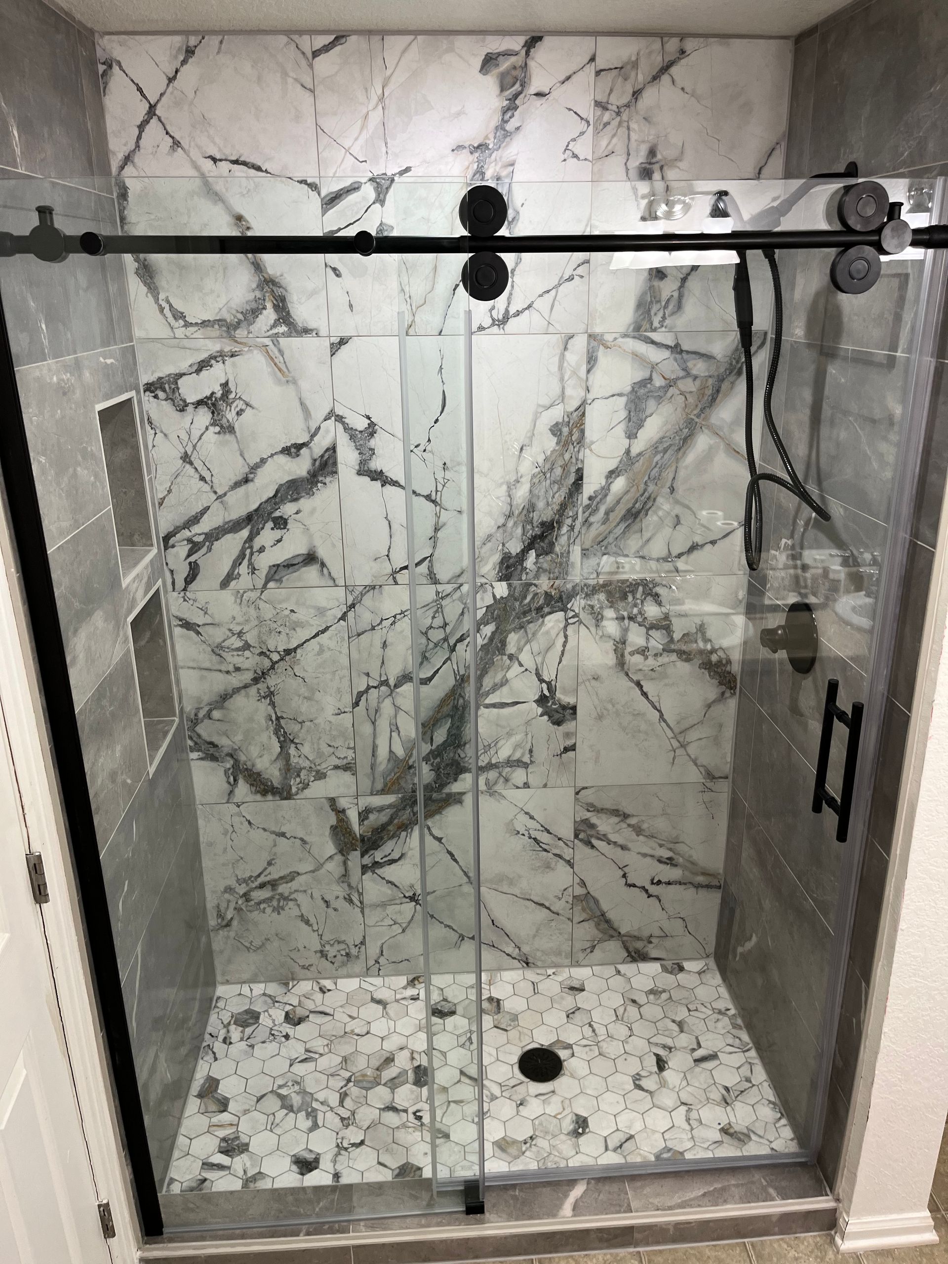 Modern marble-tiled walk-in shower with black hardware and glass doors