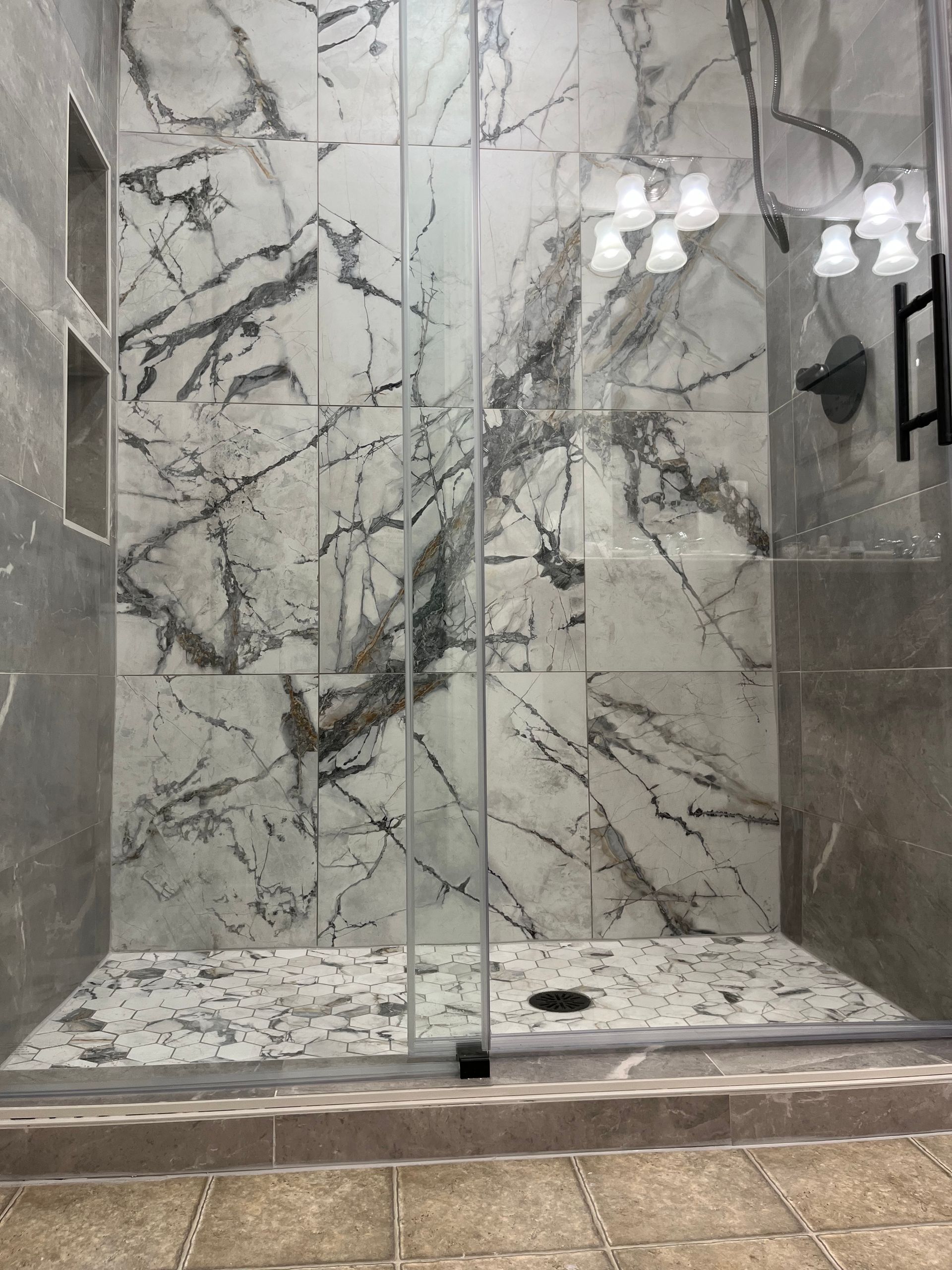 Marble-tiled walk-in shower with glass doors and chrome fixtures