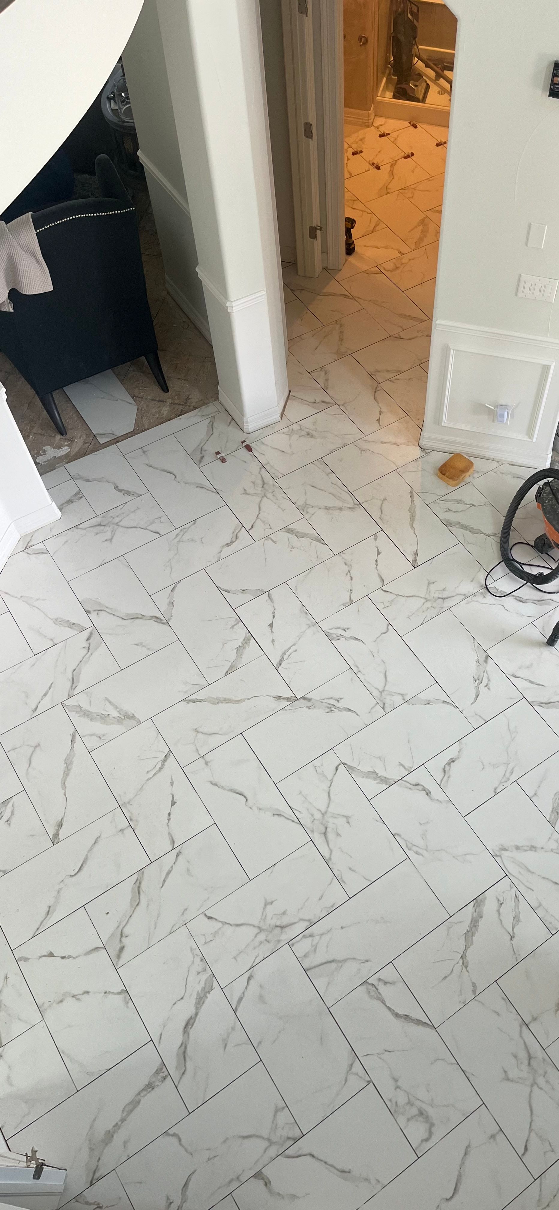 White tiled floor in a hallway with an open doorway leading to a lit room