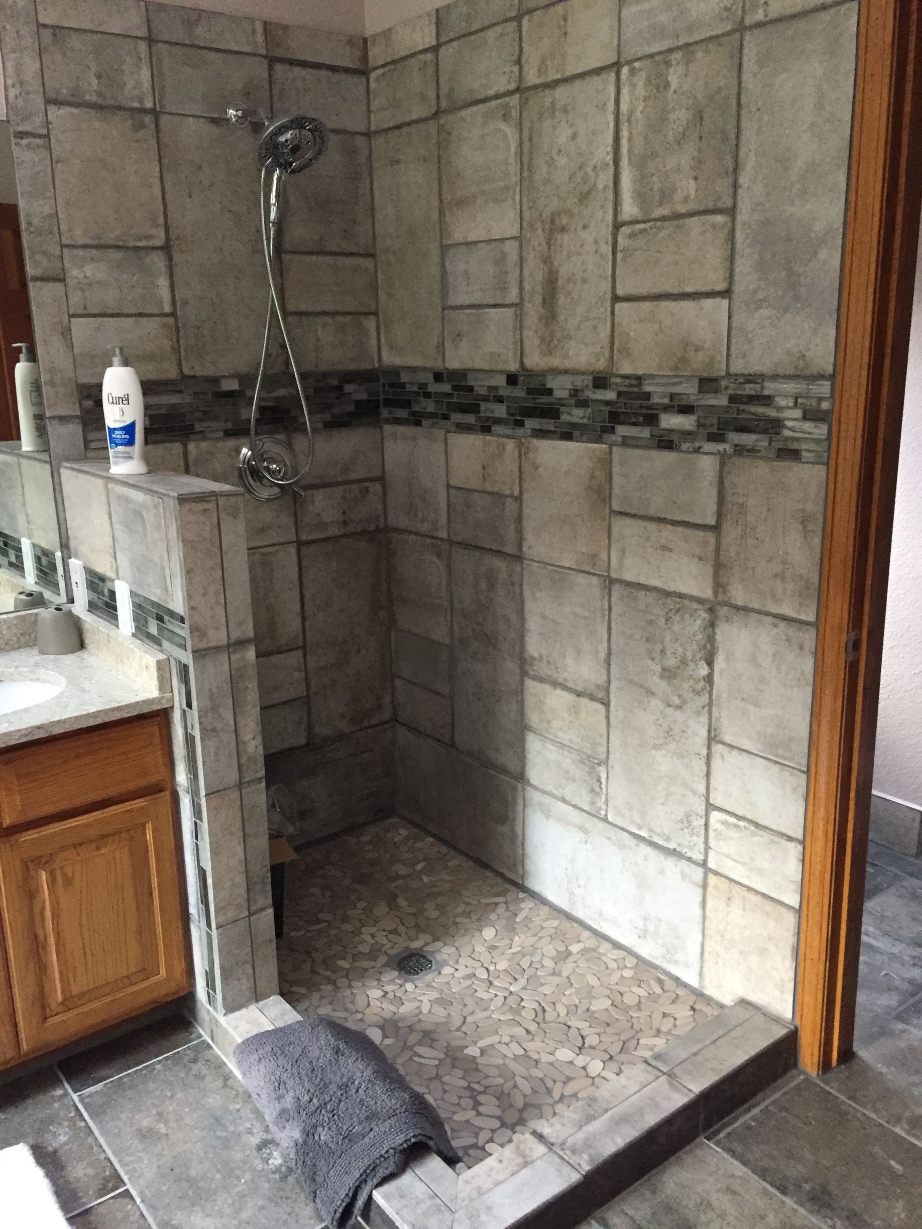 Tiled walk-in shower with chrome showerhead, built-in shelf, and bath mat on the floor