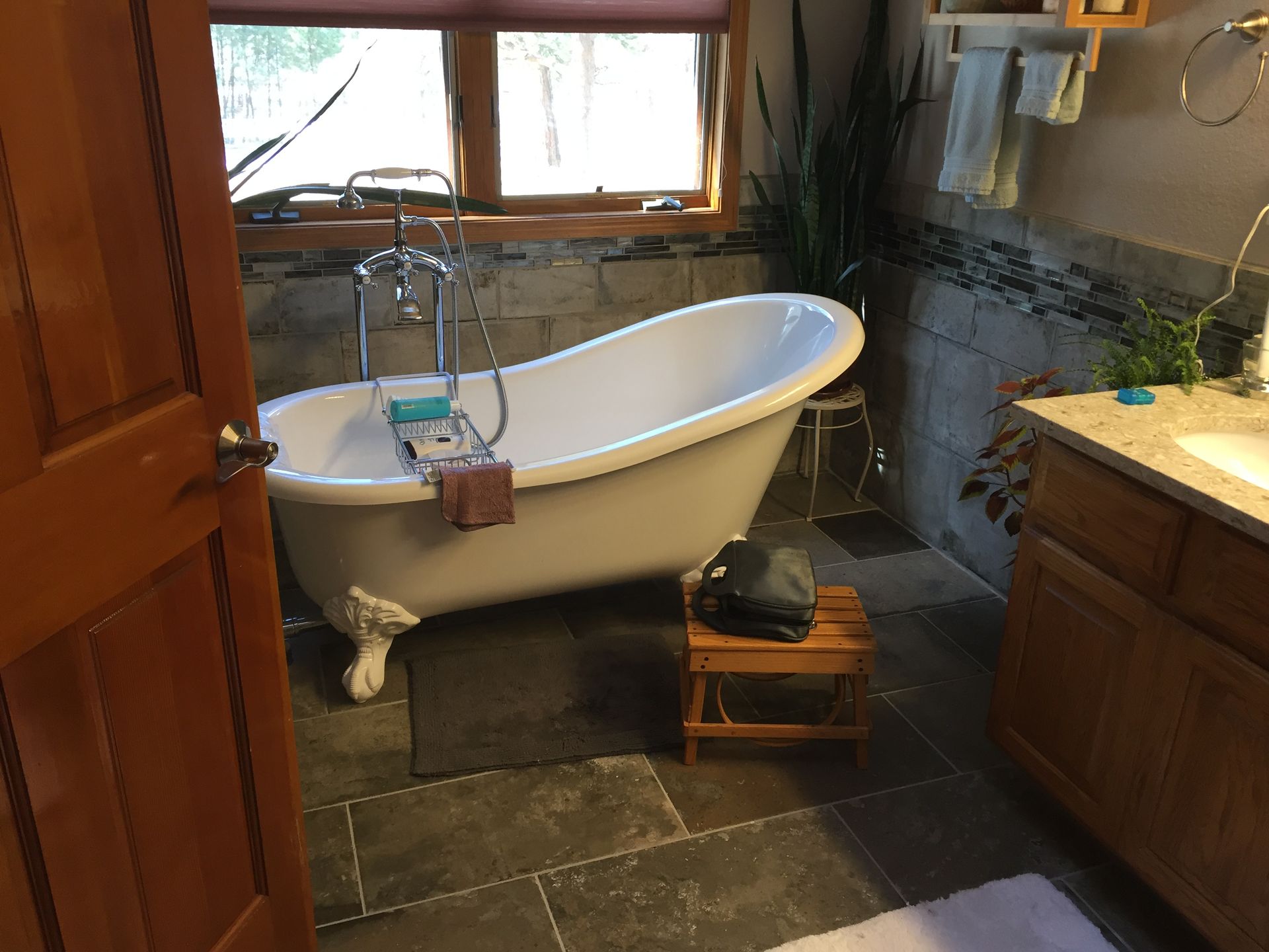 Clawfoot bathtub in a rustic bathroom, with a tiled floor and window above the sink.