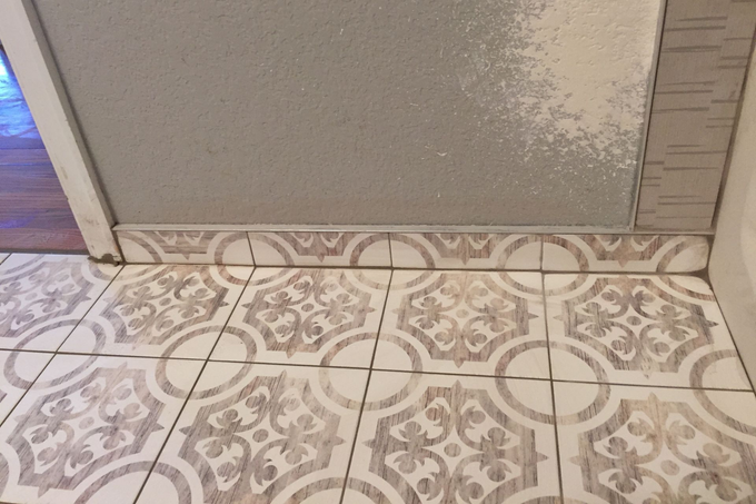 Patterned tile floor meeting a plain wall and doorway threshold indoors