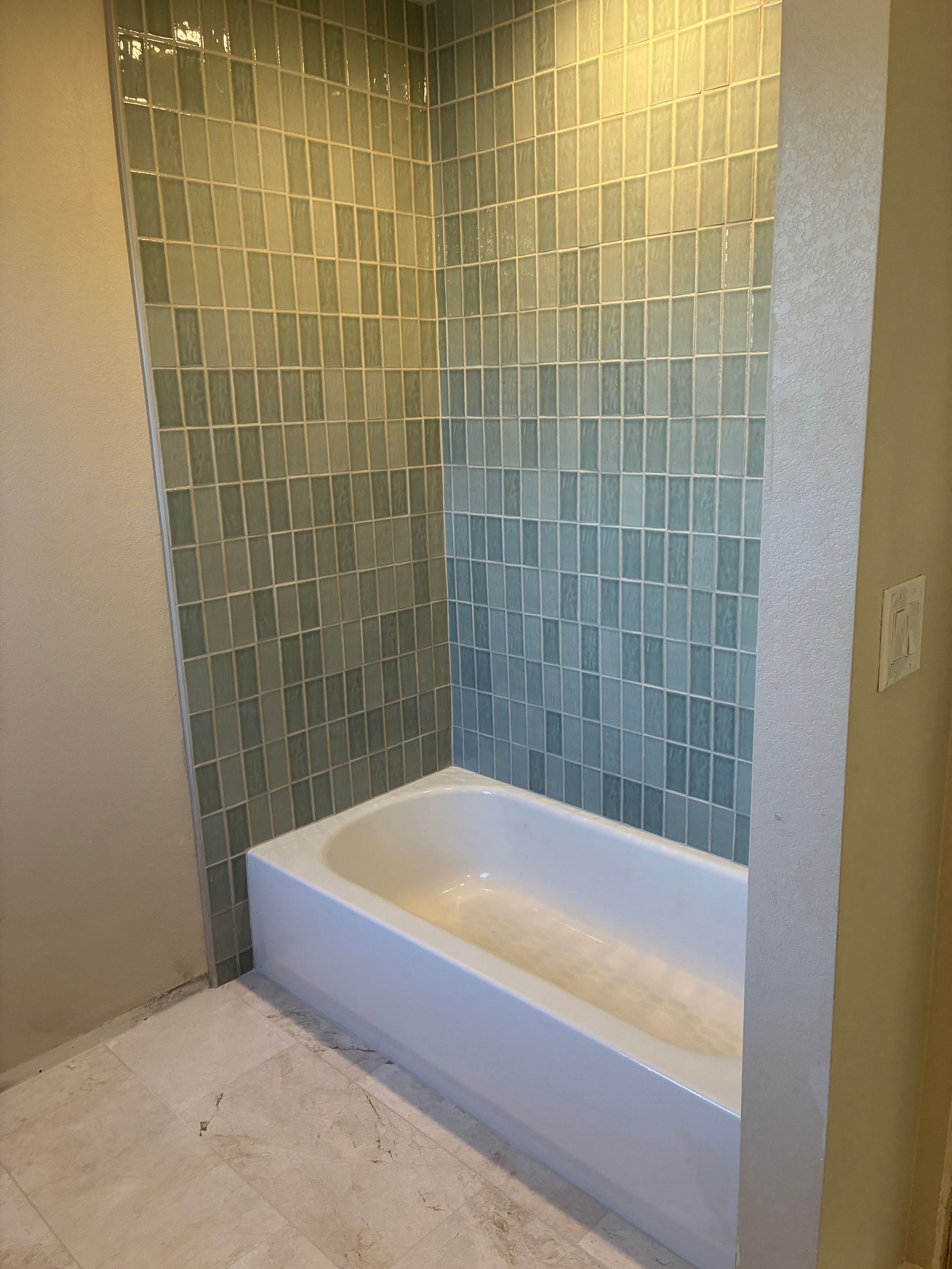 Empty bathtub alcove with green tile walls and a white tub in a small bathroom.