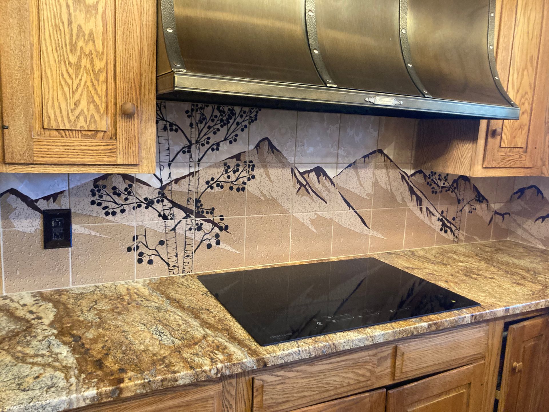 Kitchen backsplash with mountain mural behind a black cooktop and granite countertops
