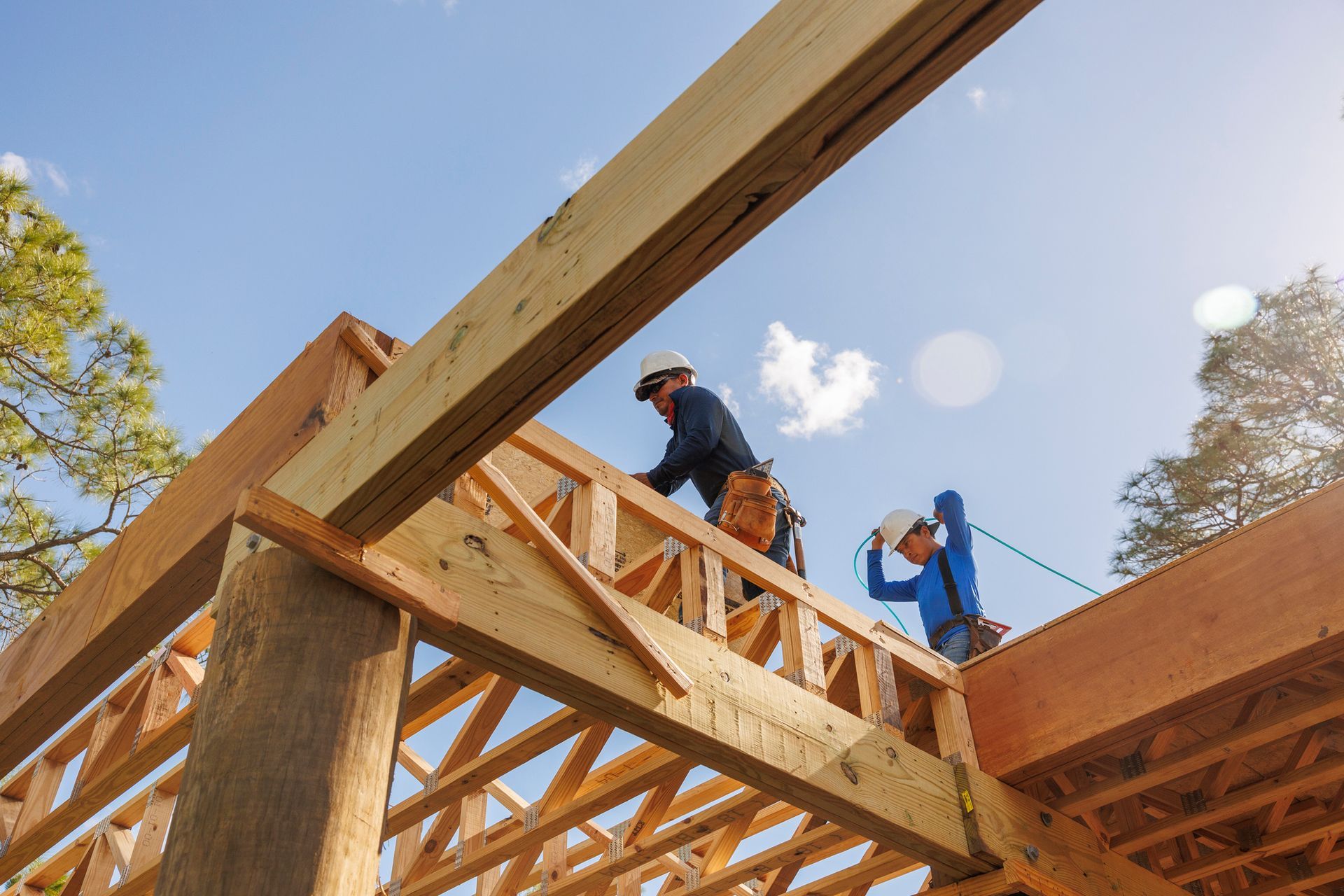 Workers install wooden roof trusses on a building site, securing beams for structural support.