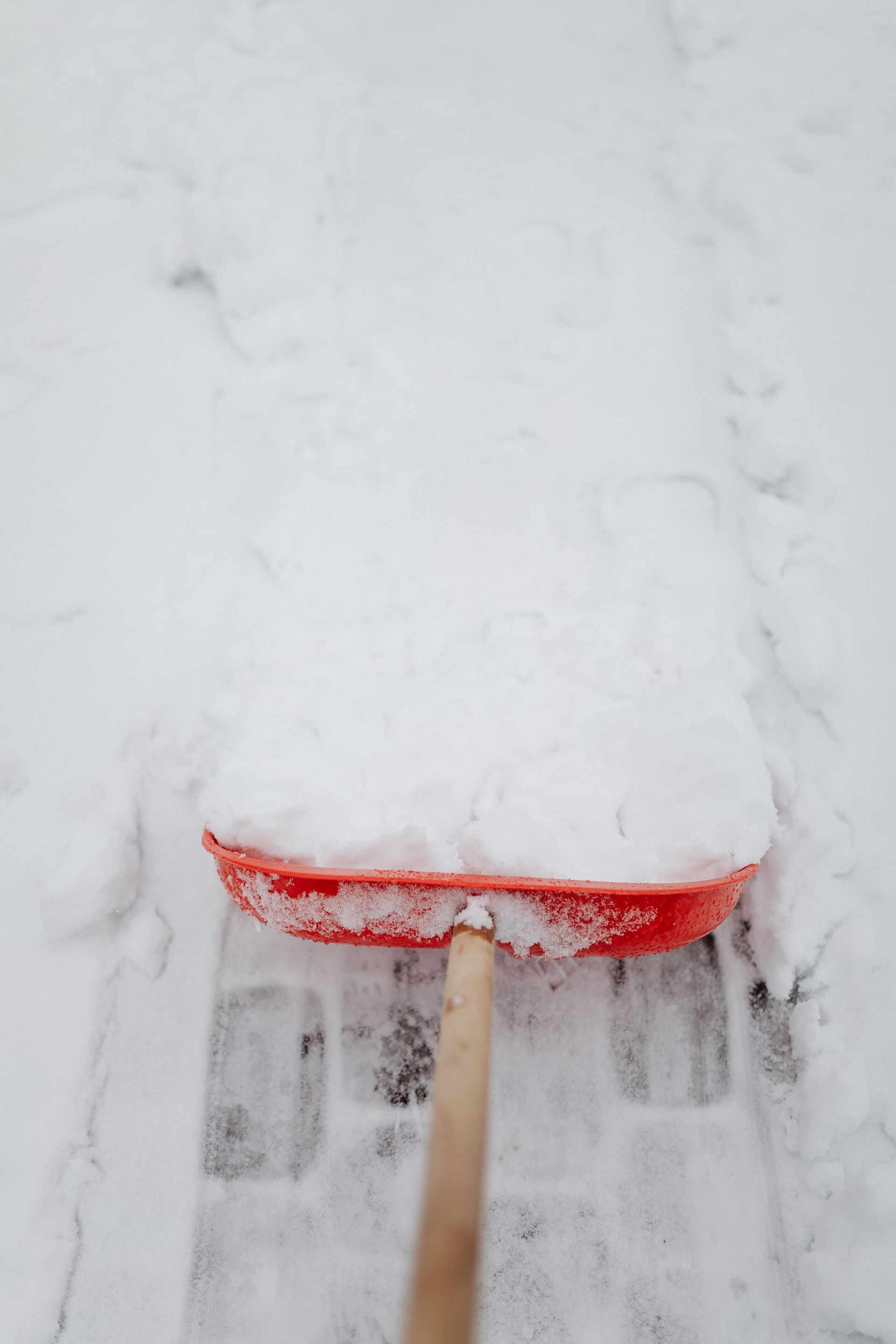 Red snow shovel pushing through deep white snow outdoors