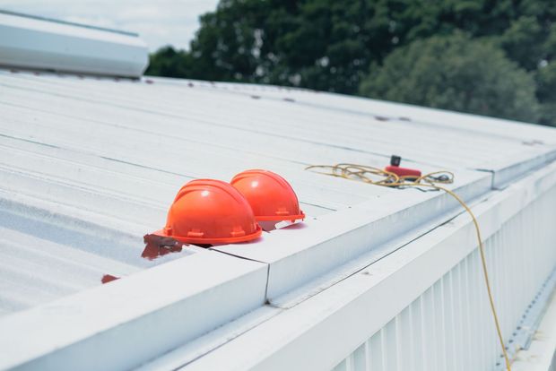 Two orange hard hats on a white rooftop beside a tool and rope harness