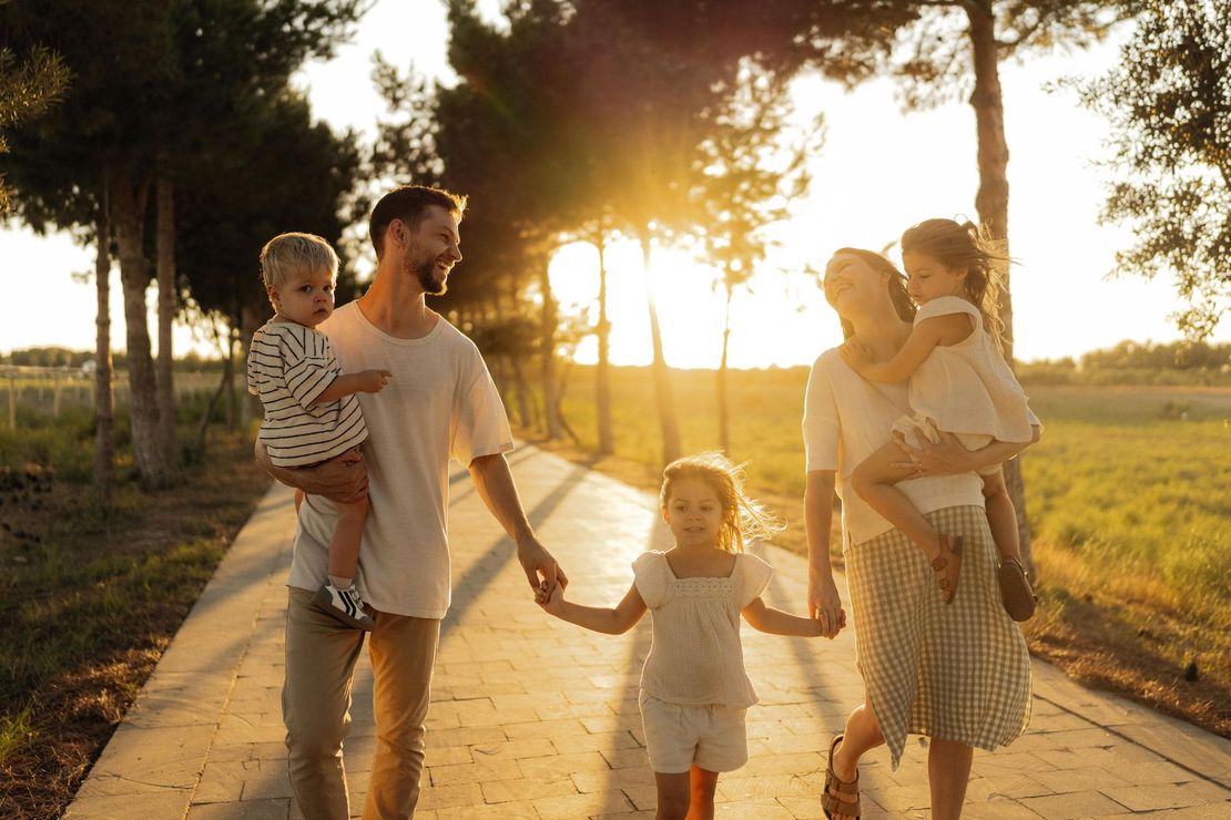 Family walking hand in hand on a sunlit path at golden hour with children and adults carrying toddlers