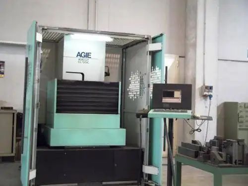 Una macchina CNC verde in un'officina con un computer su un supporto alla sua destra.