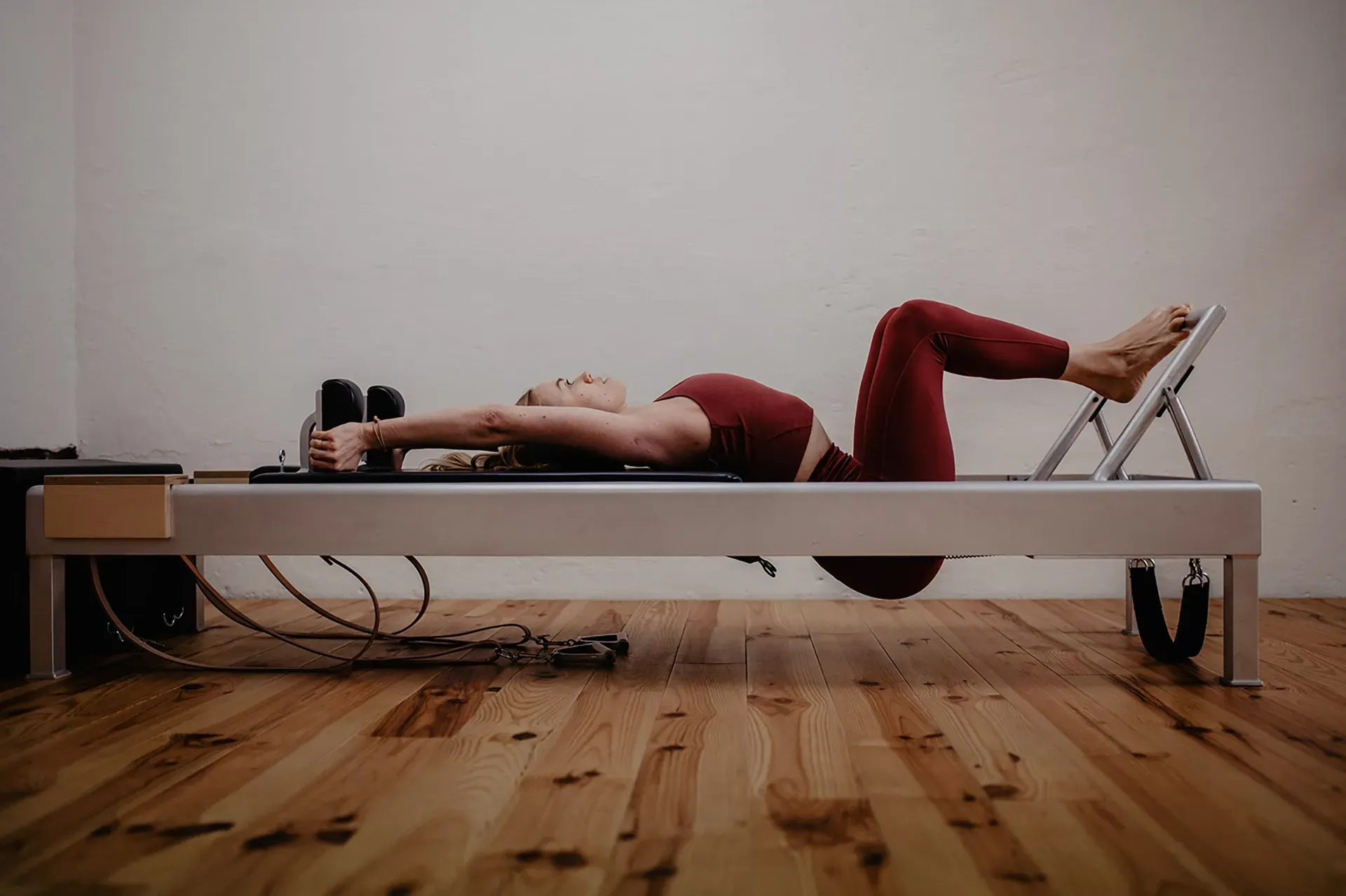 Person liegt in einem Pilates-Reformer und trägt rote Sportkleidung in einem Studio.