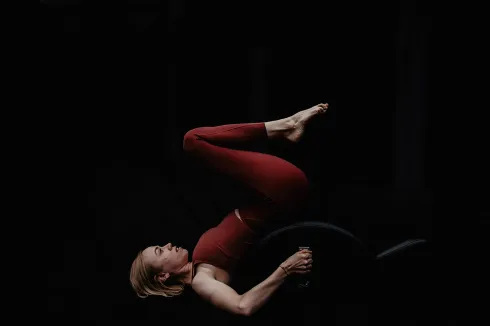 Frau in roter Sportkleidung bei einer Übung mit dem Spine Corrector vor dunklem Hintergrund