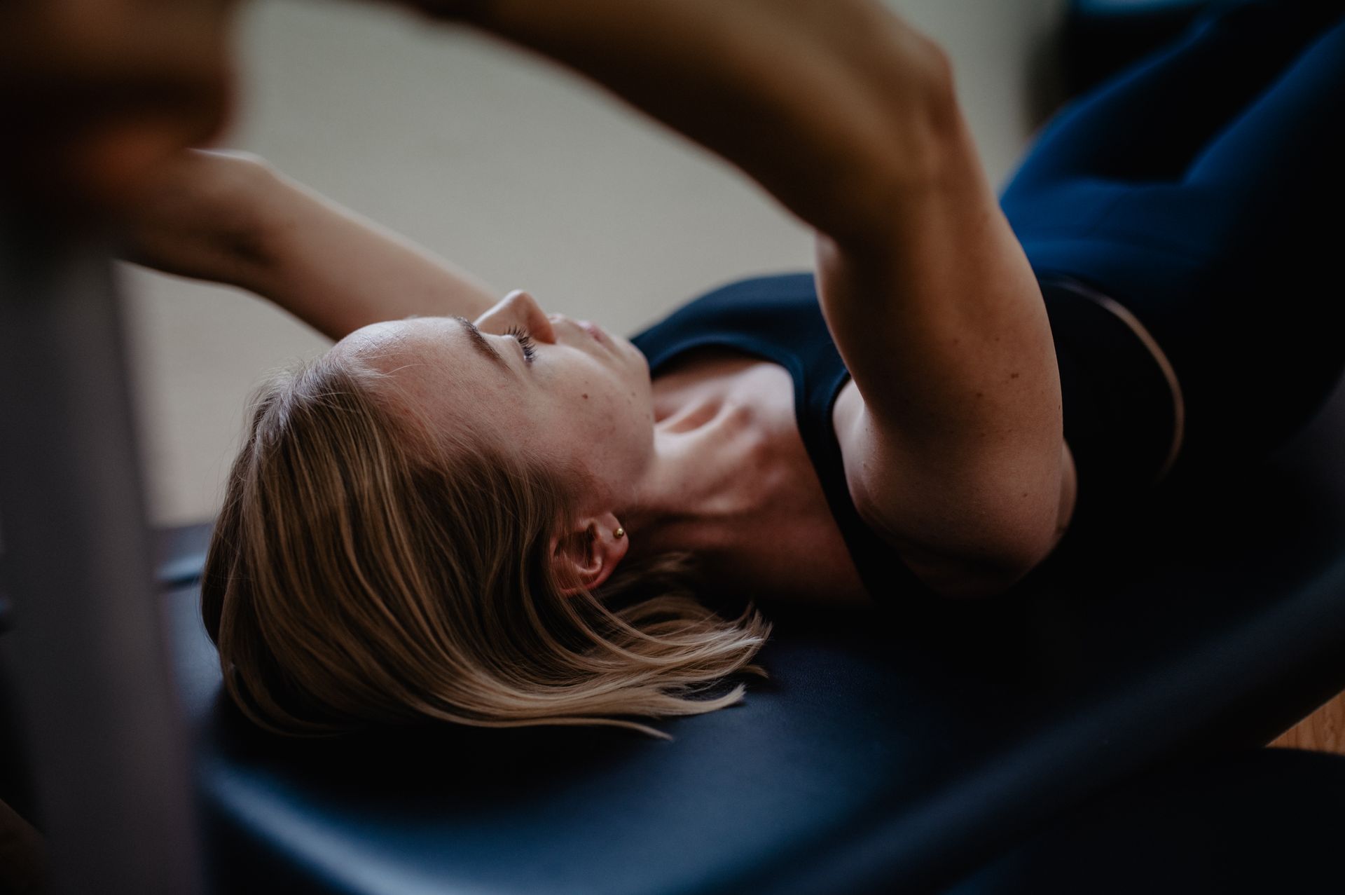 Eine Frau liegt in einer Trainingsposition auf einem Reformer und streckt die Arme über den Kopf.