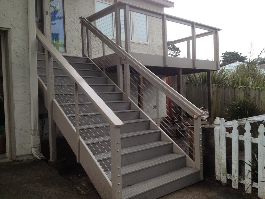 Exterior staircase with gray steps and white railings leading to a raised deck beside a house.