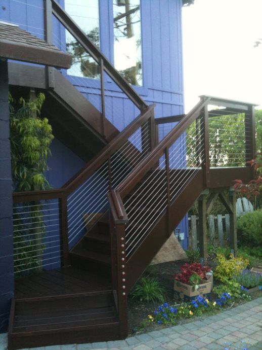 Outdoor wooden staircase with railings beside a blue building and garden path