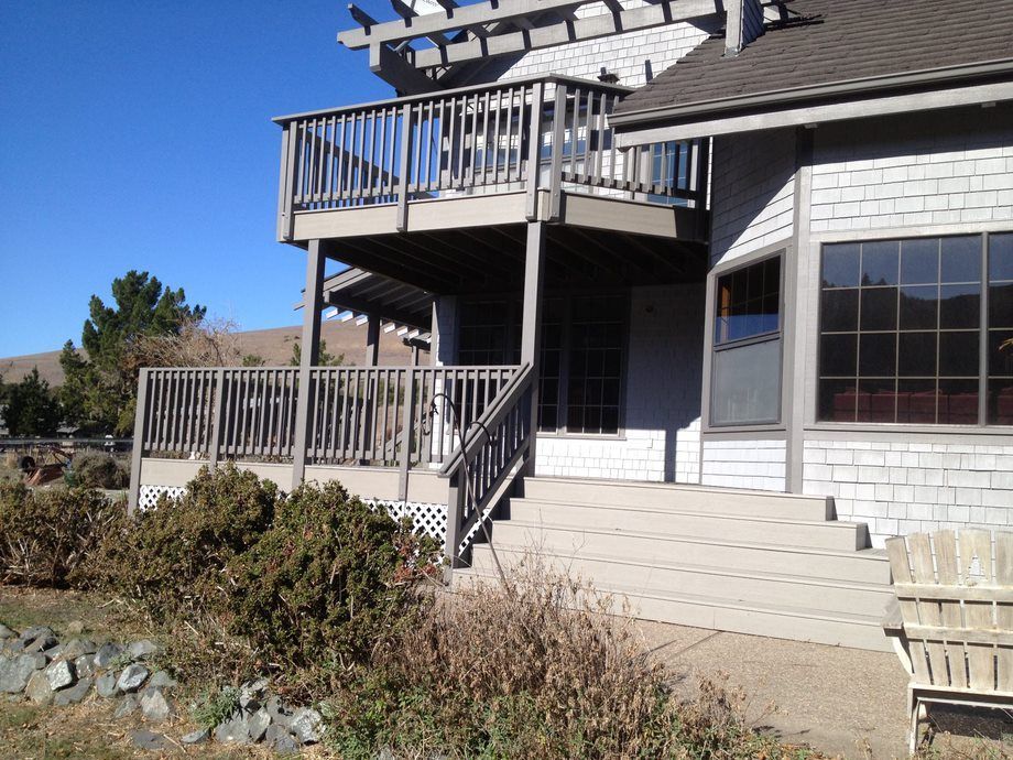 Exterior of a white house with a wooden deck, stairs, and large windows under a clear blue sky