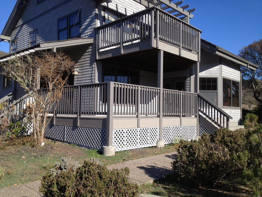 Suburban house with gray deck and stairs, surrounded by shrubs and bare trees