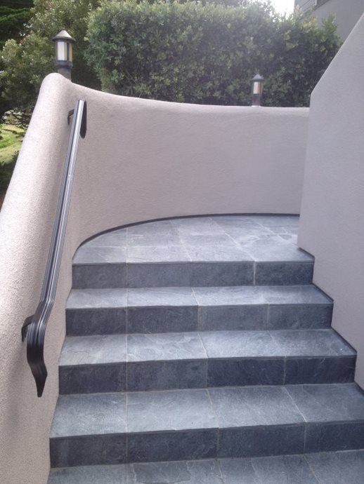 Curved outdoor staircase with gray steps, beige walls, and black handrails leading up to a terrace