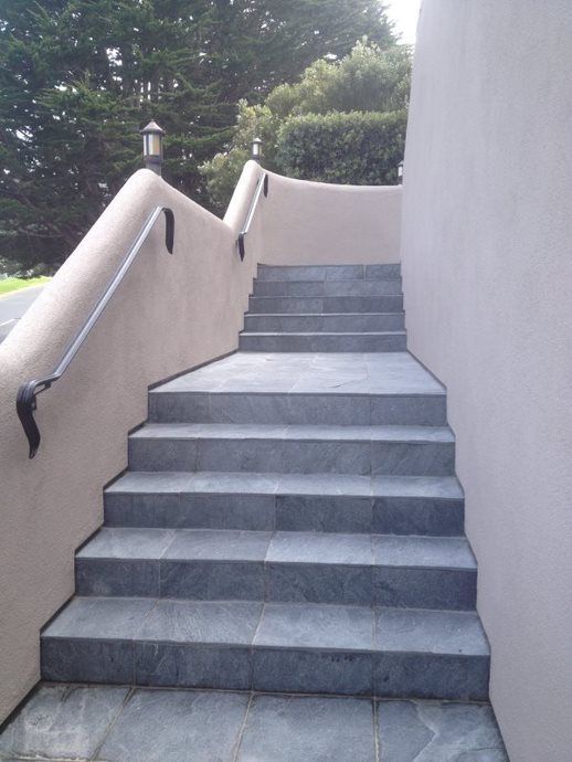 Outdoor concrete stairway with beige walls and black handrails leading up a hillside