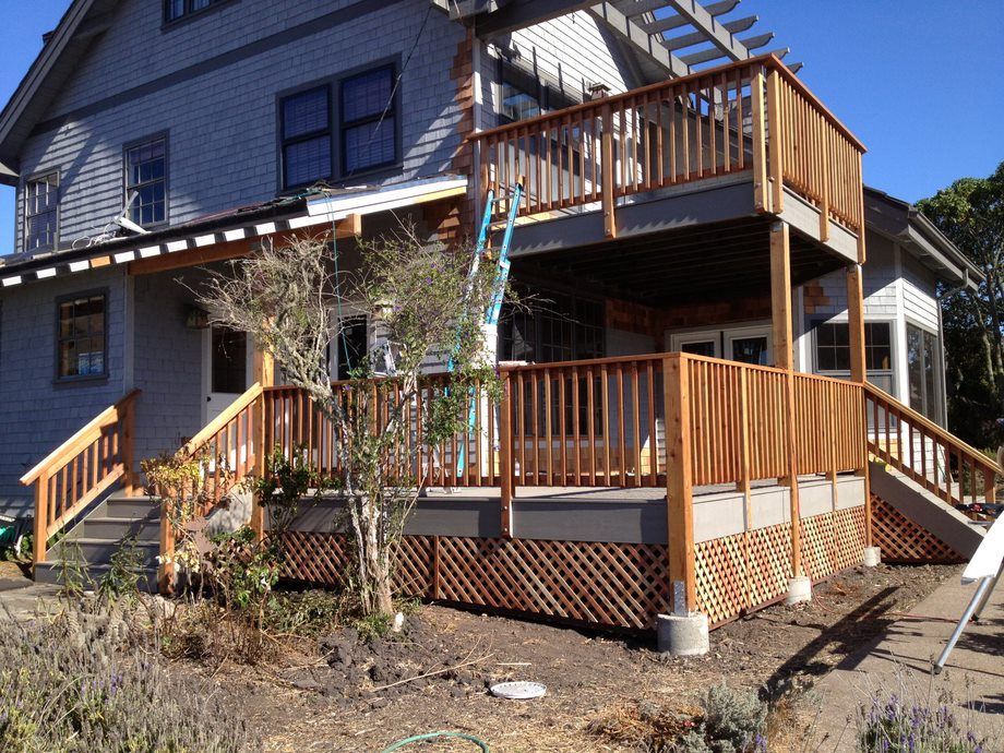 Blue house with wooden front and side porches, stairs, and railings in a sunny yard