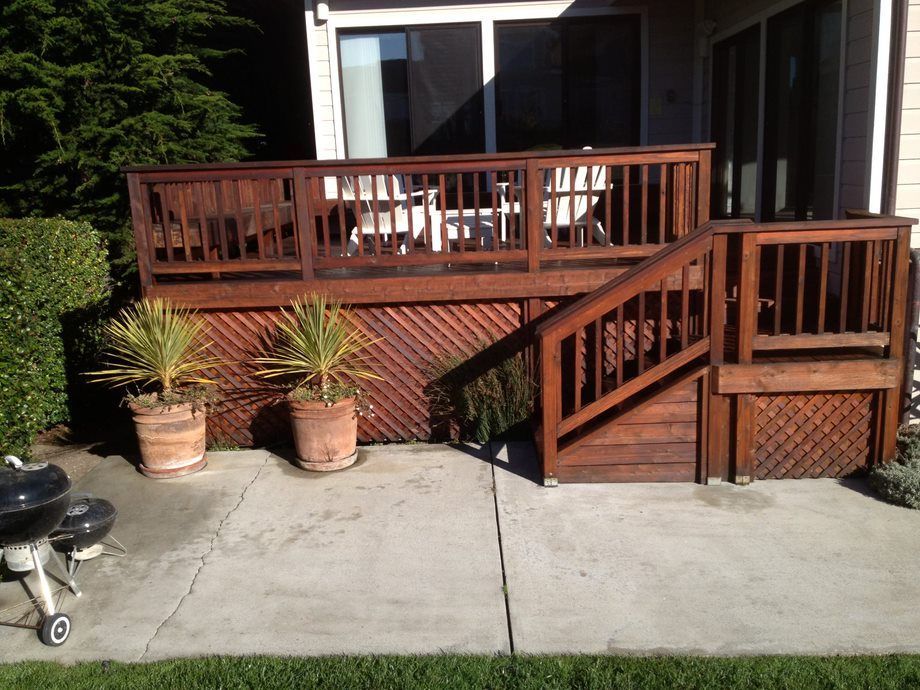 Wooden backyard deck with railing, stairs, and two potted plants beside a concrete patio.