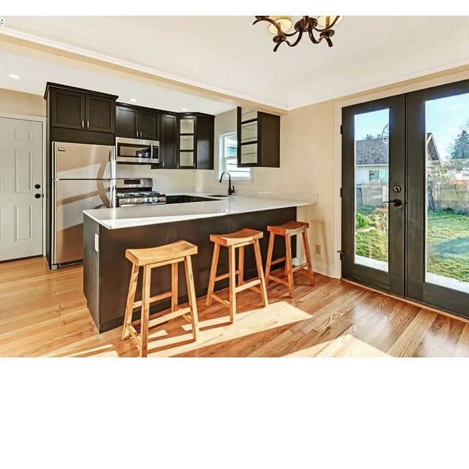 Modern kitchen with dark cabinets, white countertops, wooden stools, and large glass doors to a backyard.