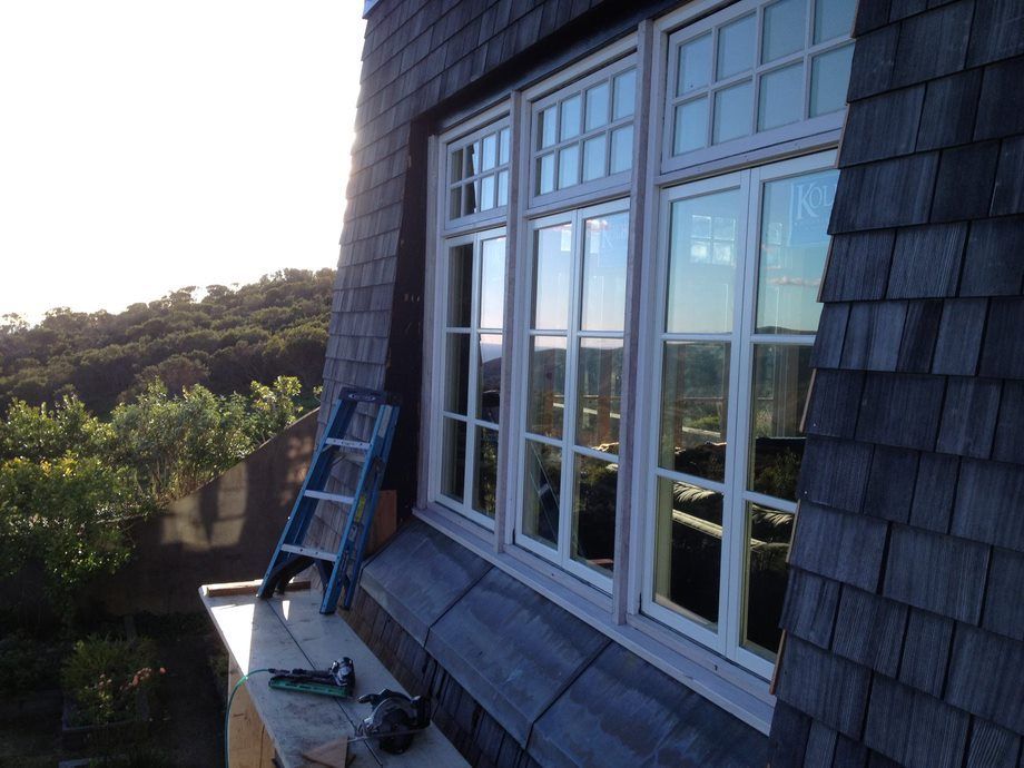 Blue-gray house window with a ladder leaning against the wall and trees in the background