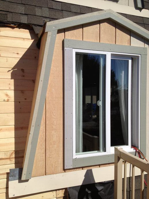 House exterior with a white-framed window and tan wood siding, bordered by gray trim.