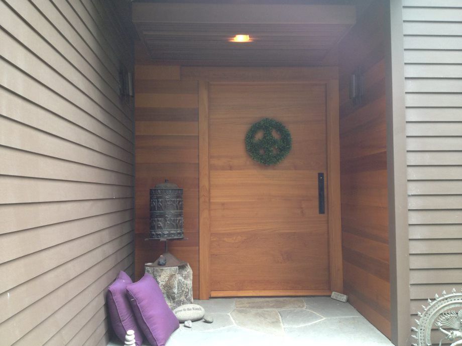 Covered front entry with wooden double doors, wreath, and purple cushions on the porch.