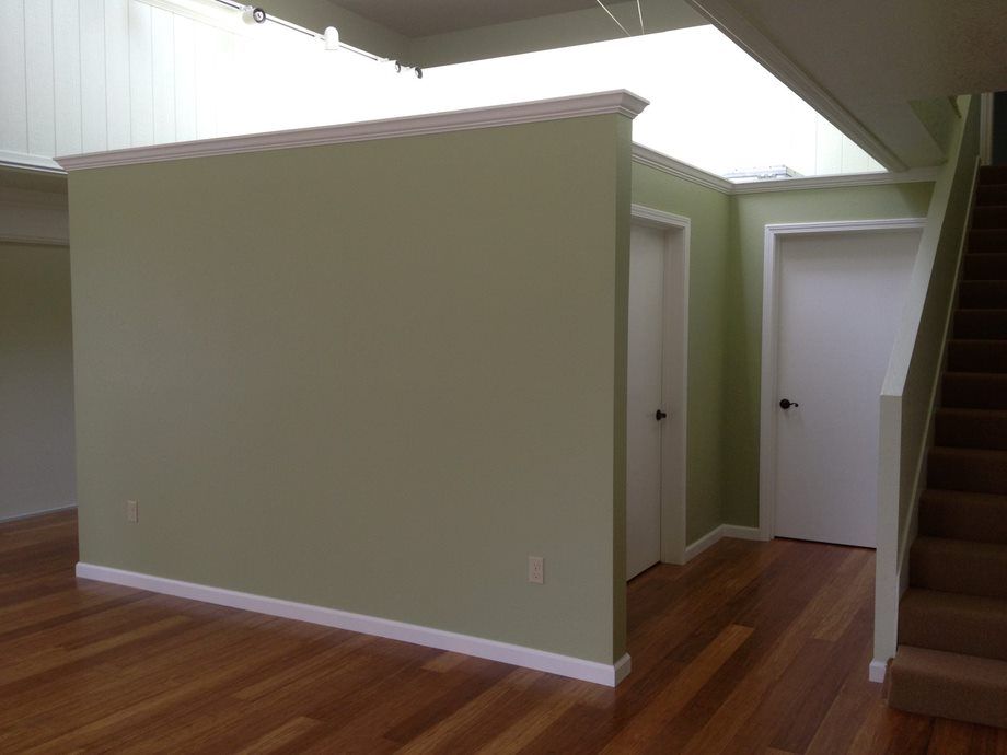 Empty modern interior with wood floors, green walls, white trim, and a staircase on the right.