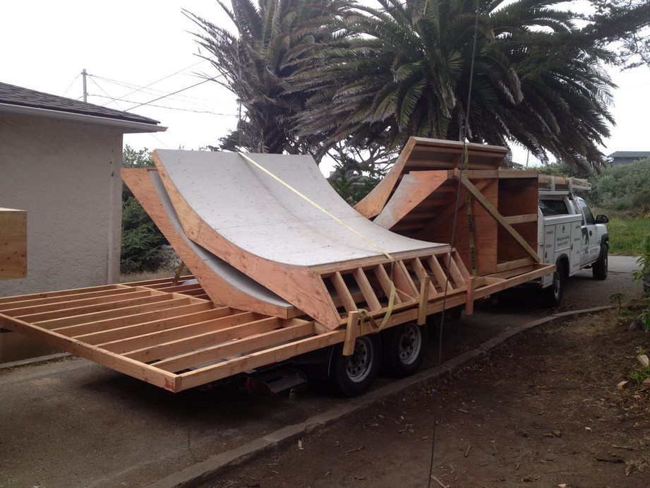 Custom-built skate ramp trailer parked beside a house, with a truck and palm tree nearby