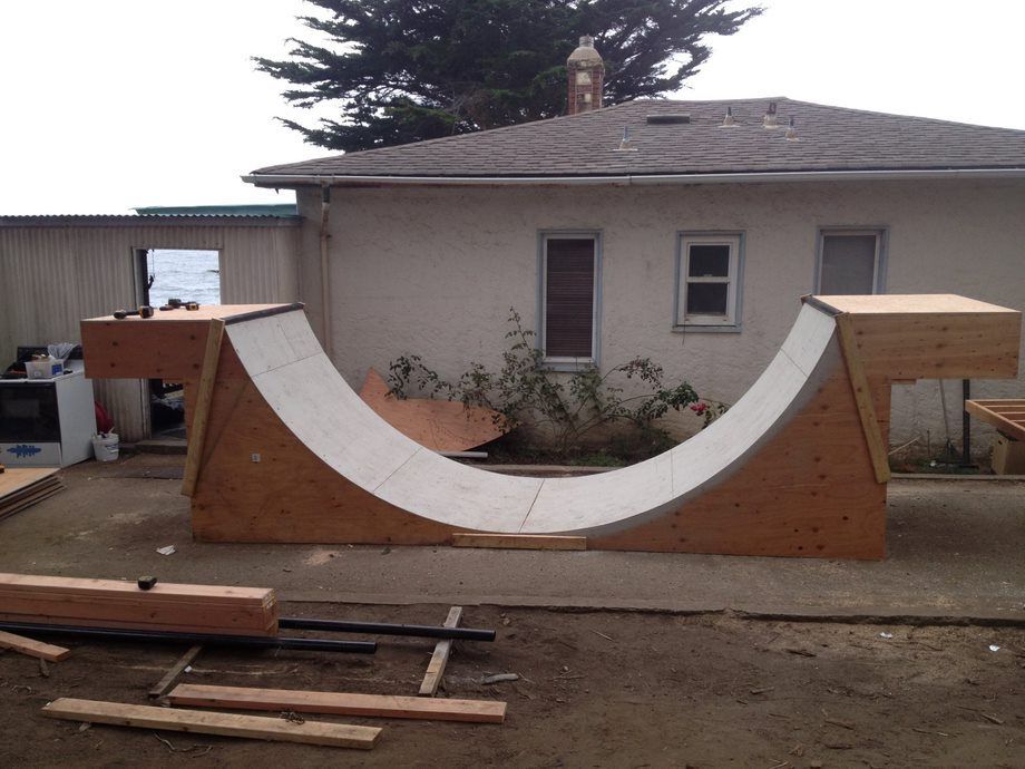 Backyard concrete skate ramp with wood sides in front of a house