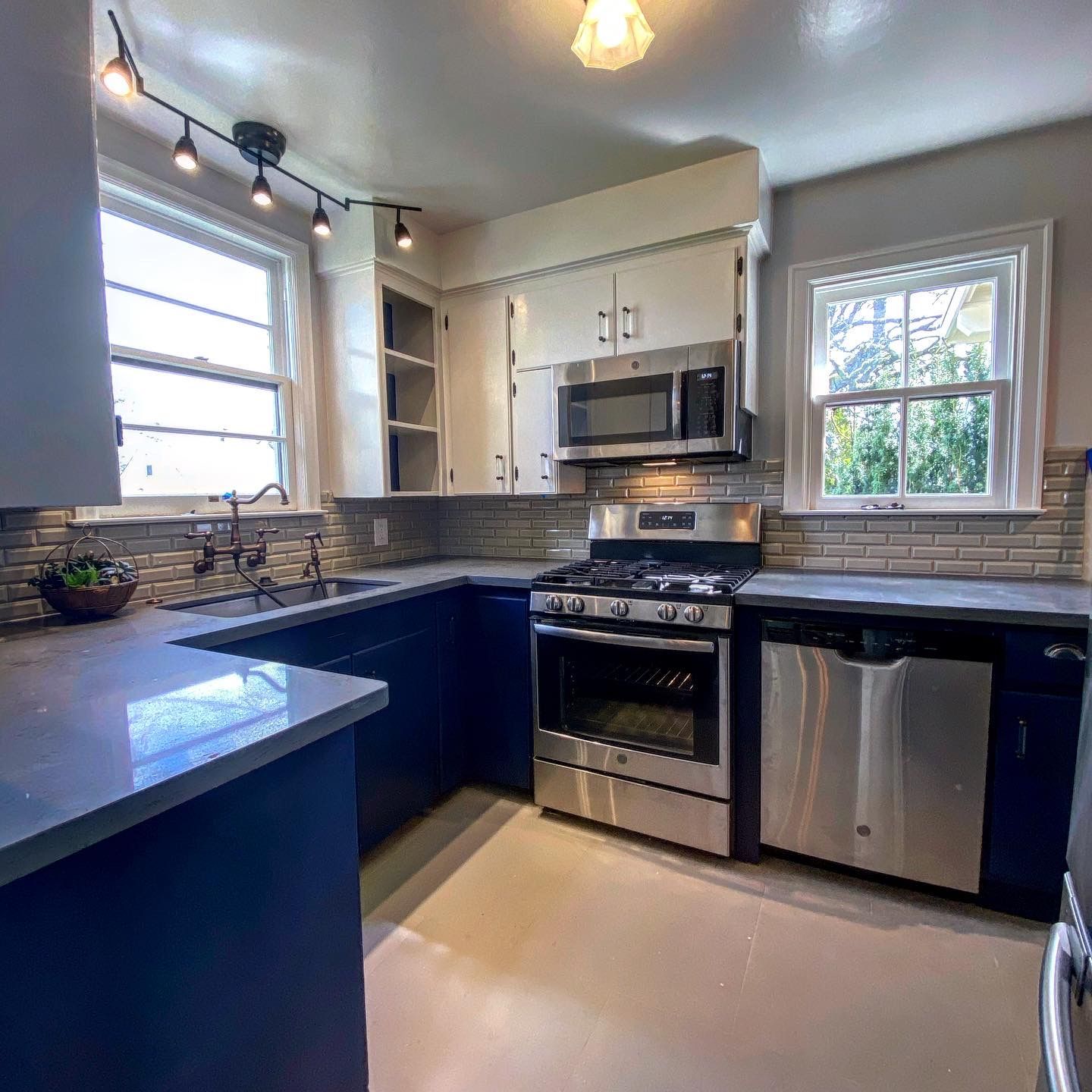 Modern kitchen with dark counters, stainless steel appliances, white cabinets, and a window over the sink.