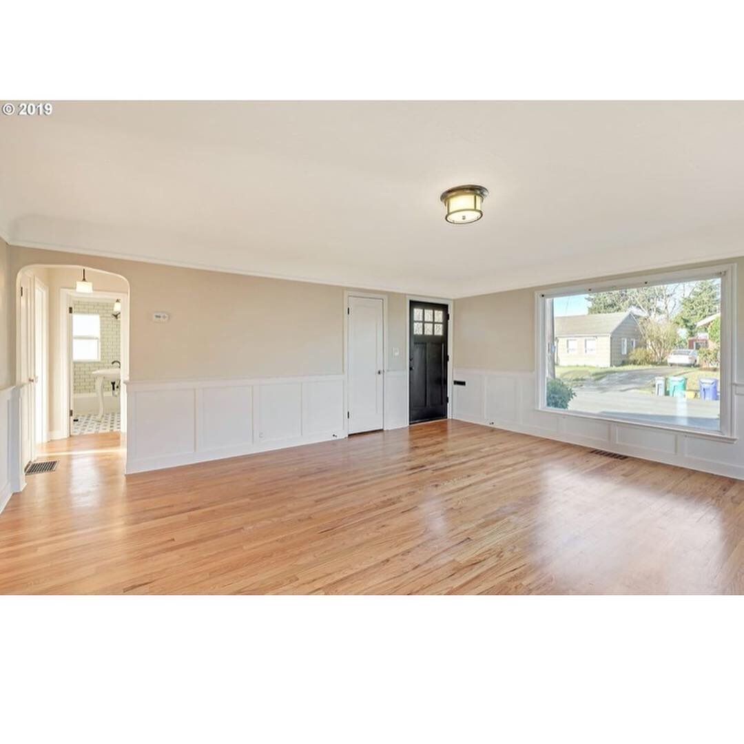 Empty beige living room with hardwood floors, black front door, and large window overlooking a street