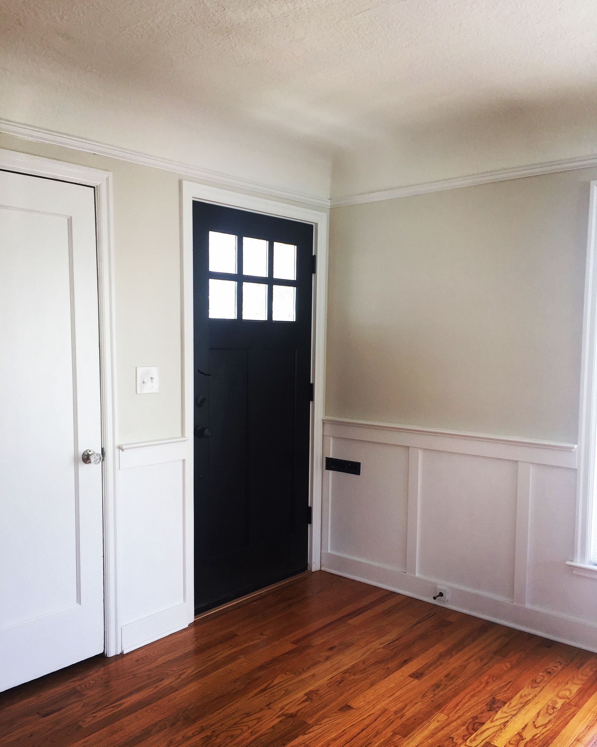 Empty room with black front door, white walls, and hardwood floor