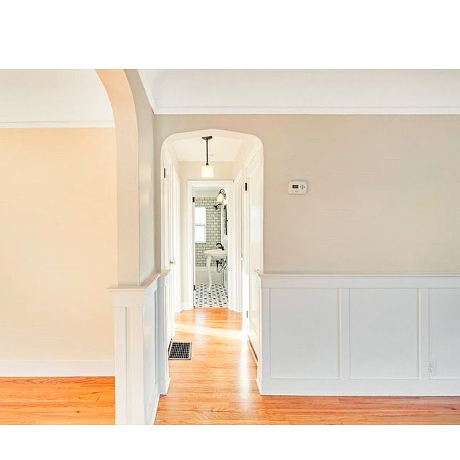 Bright hallway with white wainscoting, hardwood floors, and an arched doorway leading to a room beyond