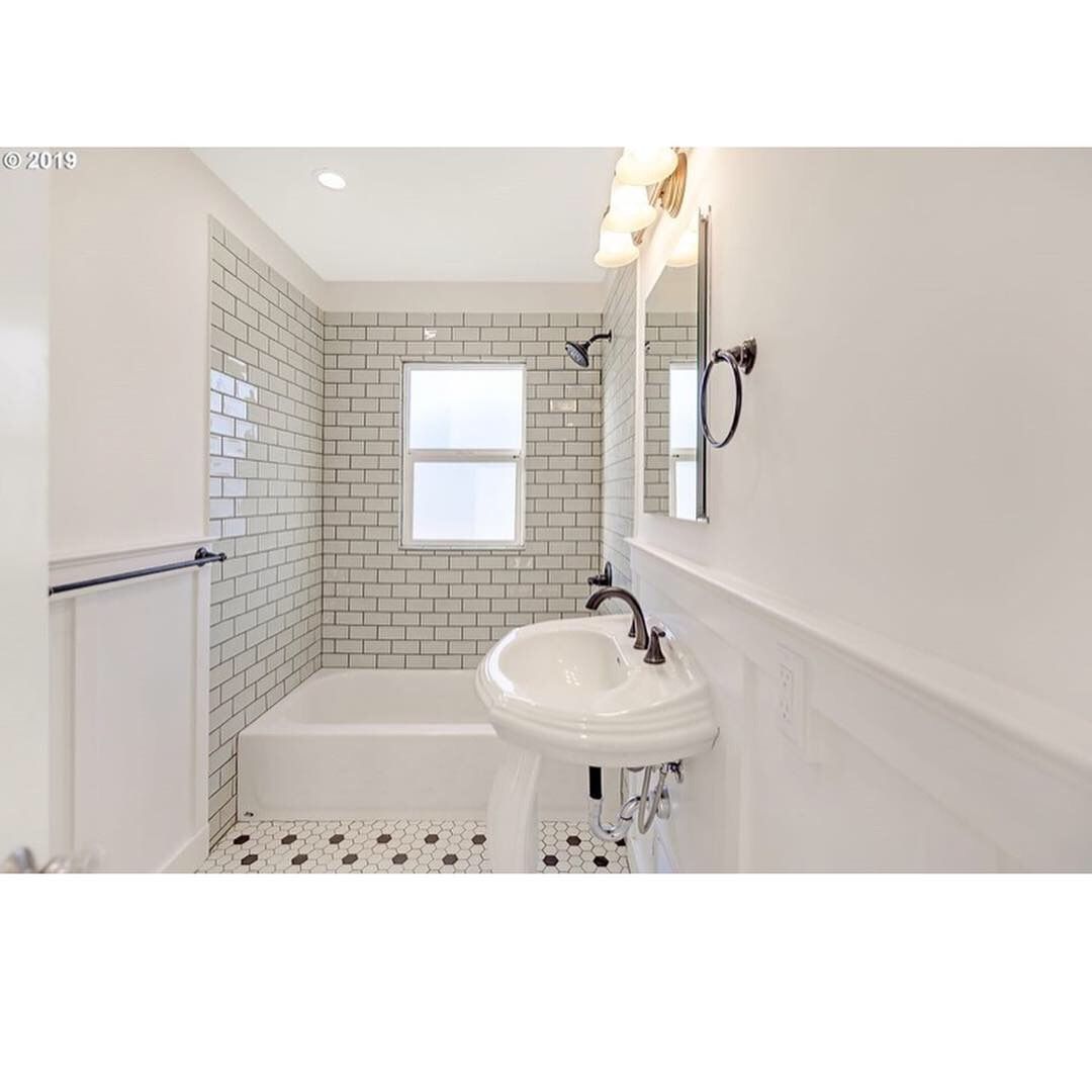 Bright white bathroom with subway-tile shower, pedestal sink, window, and patterned tile floor