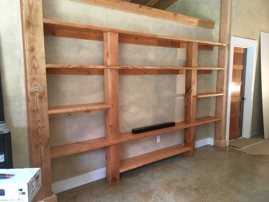 Wooden built-in shelves against a wall in an unfinished room, with concrete floor and open doorway.