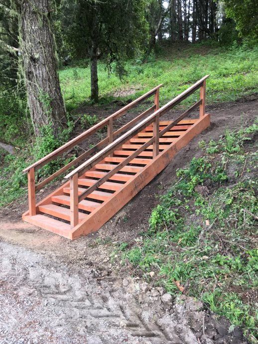 Wooden staircase with railings built into a grassy forest hillside beside a dirt path