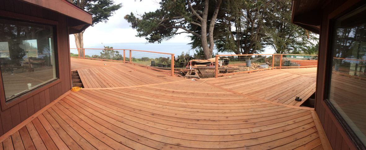 Wooden deck with railings and trees, viewed between two dark wooden buildings in an outdoor courtyard