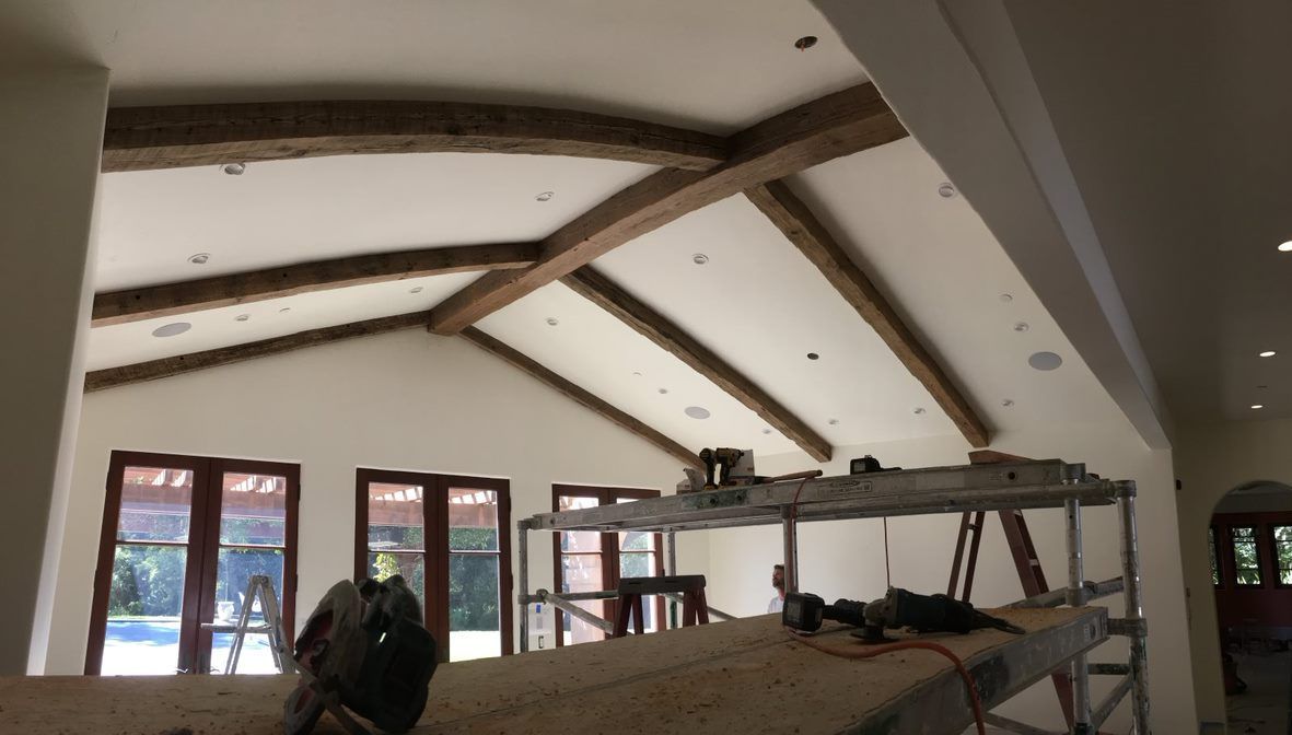 Interior room with vaulted white ceiling, exposed beams, scaffolding, and windows under construction