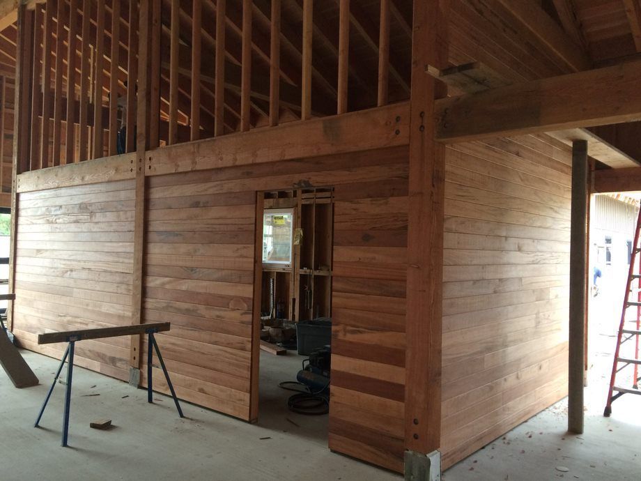 Wood-framed interior under construction with exposed studs, plywood walls, and a ladder at the doorway