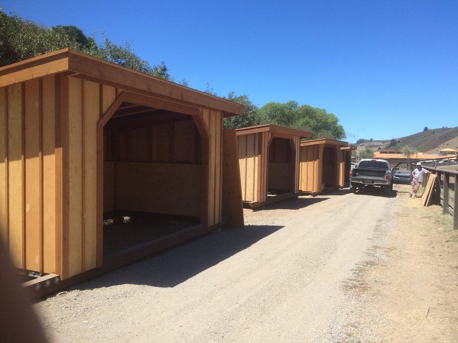 Row of wooden sheds along a dirt road under a blue sky, with a parked pickup truck nearby