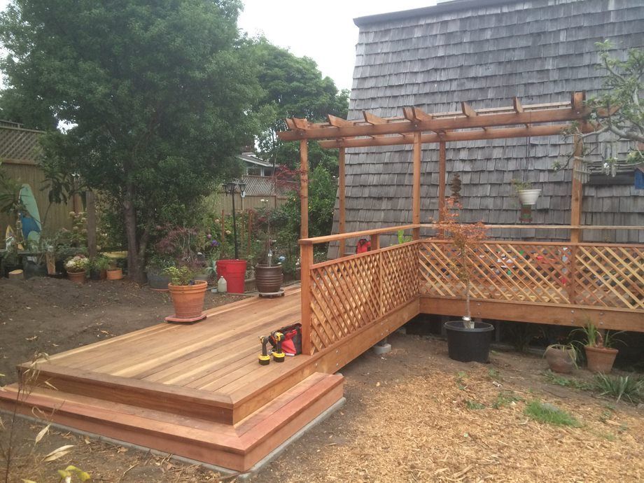 Wooden wheelchair ramp and deck beside a house, with lattice railings and potted plants in a yard.