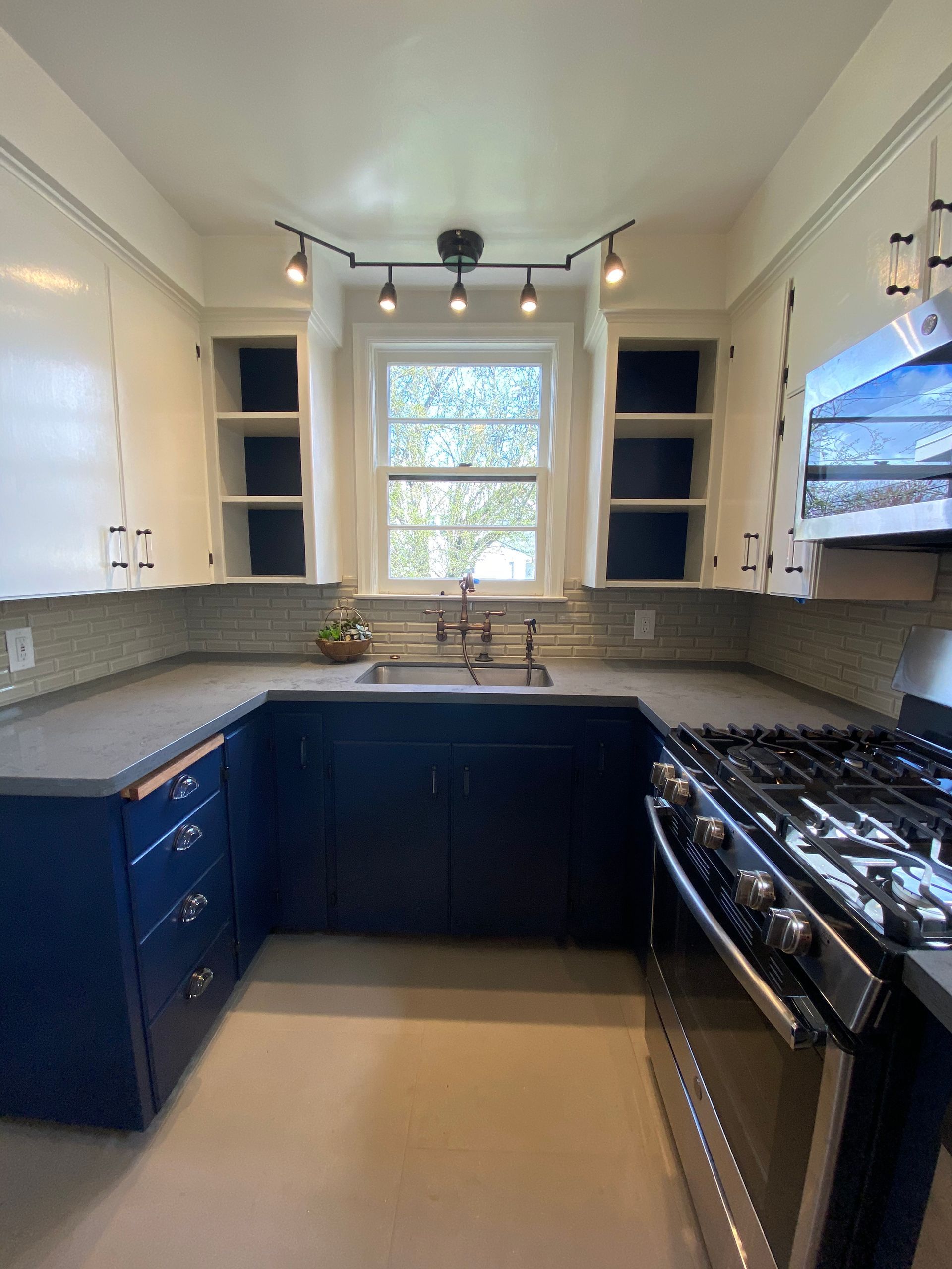 Compact U-shaped kitchen with dark blue cabinets, gas stove, and window over the sink