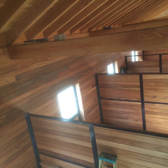 Wood-paneled attic with exposed beams and open railings around bright windows.