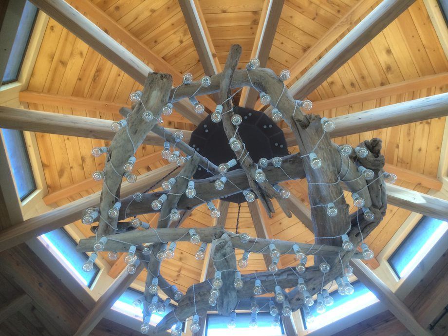 Large circular metal chandelier beneath a wooden vaulted ceiling, viewed from below