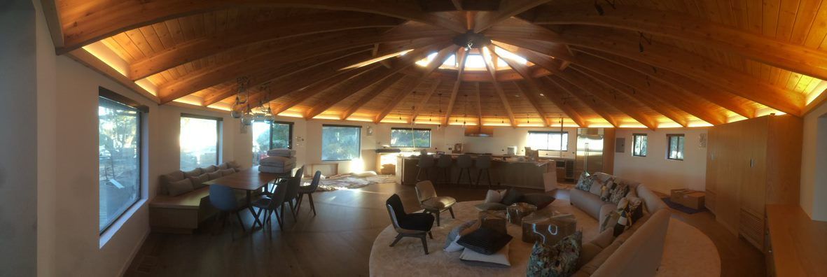 Wood-paneled living room with sofas, tables, and large windows under a vaulted ceiling