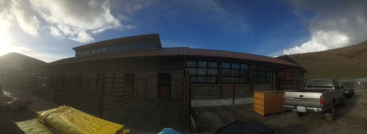 Sunny exterior of a brick building with dark windows, viewed from a courtyard with bins and distant hills.