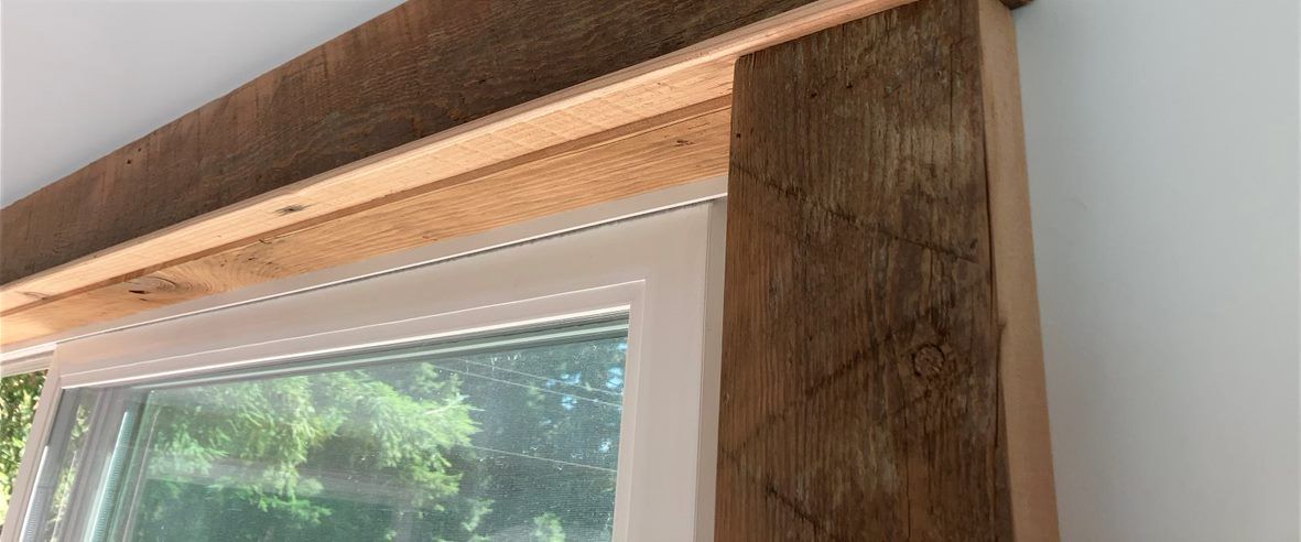 Wood-framed window with a light wood beam above and greenery visible outside